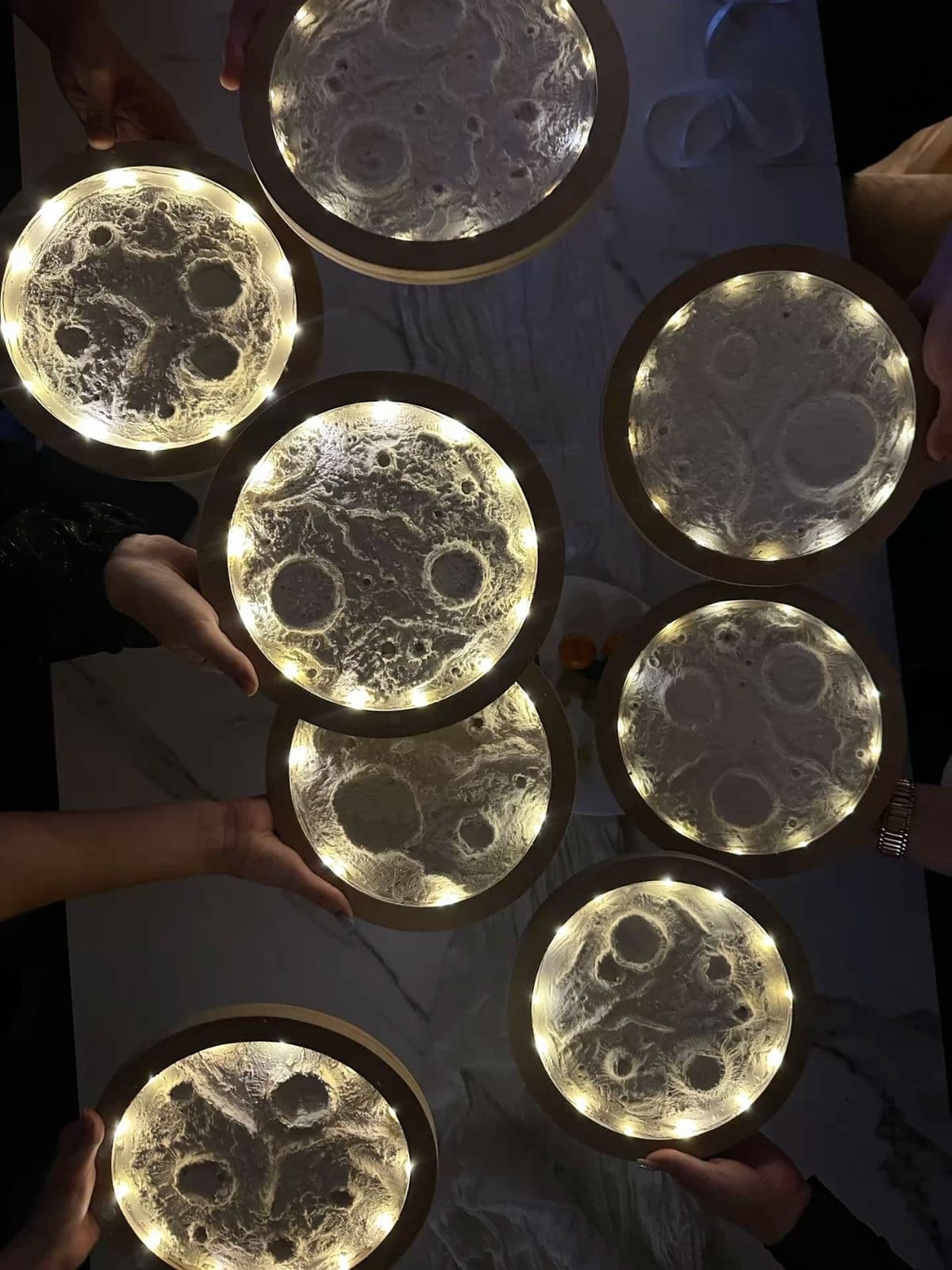 Multiple guests holding finished glowing moon artworks overhead